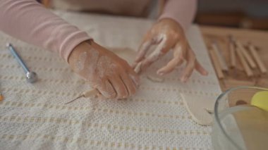 Kadın, çömlek atölyesinde kilden kesme aleti ile heykel yapar; dikkatli sabır işçiliği.