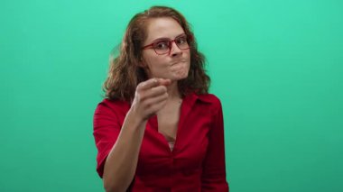 Kırmızı gömlekli ve gözlüklü genç bir kadın öfkeyle yeşil arka plan duvarını işaret ediyor anlamlı bir jest ve kararlı bir ifadeyle..