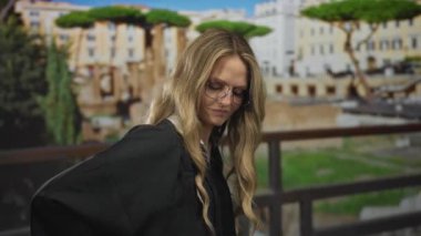 Sırtı ağrıyan bir kadın, Roma sokaklarına bakan üniformalı genç sarışın bir yargıcın yanında harabelerde duruyor..