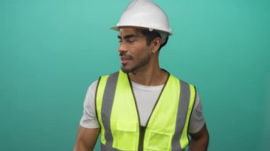 Beyaz kasketli ve yansıtıcı yelek giyen İspanyol genç adam turkuaz stüdyoda onay verdi..