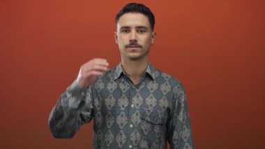 Kalıplı gömlekli genç İspanyol adam, izole edilmiş kırmızı arka plana karşı elleriyle gözlerini kapatıyor..