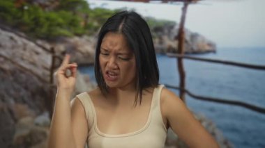 Genç Çinli kadın deniz kenarında enerjik bir şekilde kutlama yapıyor. Sahilde manzaralı deniz manzaralı bir yerde neşe ve kararlılığını ifade ediyor..