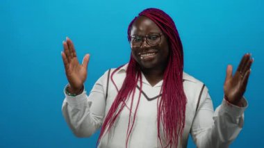 Mavi arka planda örgülü saçları olan, gözlüklü ve beyaz gömlekli neşeli ifadesini ve canlı tarzını vurgulayan bir kadın..