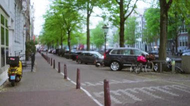 Park halindeki arabalarla, bisikletlerle ve bulutlu gökyüzünün altında ağaçlarla kaplı kaldırımlarla çevrili bir Avrupa şehrinin bulanık sokaklarıName.