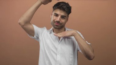 Şeftali stüdyosuna karşı ellerini kullanarak yüzünü çerçeveleyen genç İspanyol adam, alnında ve çenesinde avuçlar göstererek neşeli ölçü;.