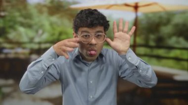 Gözlüklü İspanyol genç adam yeşil ormanda elini kaldırıyor ve yapraklı gölgeliğin altında elini kaldırıyor..