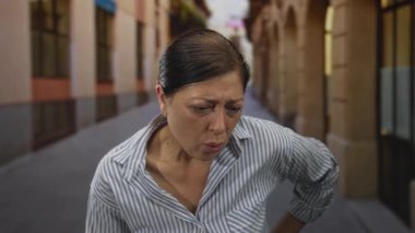 Kadın, tarihi bina cepheleriyle dolu eski şehir sokağında öne doğru eğilerek burun ve kaşlarını çatıyor; iğrenme.