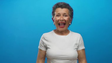 Gri saçlı, canlı mavi bir arka plana gülümseyen, mutluluk ve pozitiflik saçan son sınıf öğrencisi kadın..