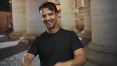 Genç adam gülümsüyor ve kalbi şekillendiriyor. Geceleri eski bir kasaba sokağında, arka planda sütunları olan, sıcaklığını ve şehir cazibesini gösteren eller..