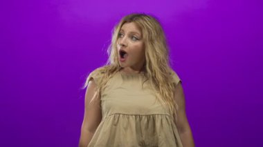 Sarı saçlı, ağzı açık, mor stüdyoda bej bluz giyen bir kadın..
