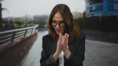 Şehir sokaklarında kutlama yapan bir kadın, neşeli bir ortam olduğunu düşündüren, yumruklarını kaldırarak, gözlük takarak ve spor ceket giyerek mutluluğunu ifade ediyor..