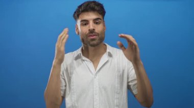 Genç, ağzı açık bir İspanyol adam, parlak mavi stüdyoda ellerini kaldırdı ve şaşırmış ifade; sürpriz şaşkınlık.