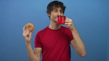 Adam kırmızı bardağı kokluyor ve mavi stüdyoda jöleli donut tutuyor; keyif düşkünlüğü..