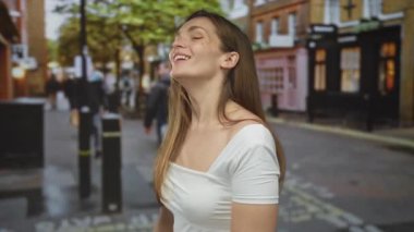 Genç beyaz kadın elini uzatır kalabalık bir sokakta dükkanlar ve ağaçlarla dolu; sıcak karşılama.