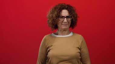 İspanyol kadın reddedildiğini bir jest ve somurtmayla ifade ediyor, canlı kırmızı bir duvara karşı duruyor, gözlük takıyor ve üstünkörü giyiniyor, güçlü bir duygusal tepki veriyor..