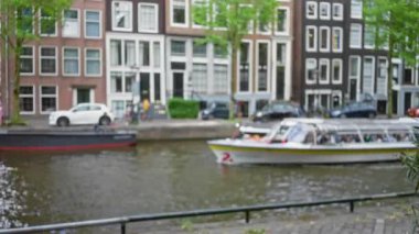 Işıldayan suya yansıyan tarihi binalarla pitoresk Amsterdam 'da gezinen bir kanal turu teknesinin bulanık görüntüsü..