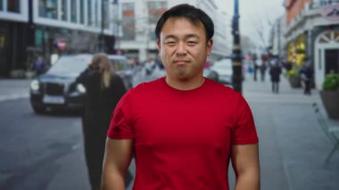 Kırmızı gömlekli genç adam arka planda binalar ve araçlarla kalabalık şehir sokaklarında hareketli bir şehir atmosferini taşıyor..