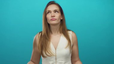 Beyaz bluzlu genç beyaz kadın kulaklarını mavi stüdyoda parmaklarıyla kapatıyor..