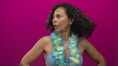 Mavi mayo giymiş orta yaşlı İspanyol bir kadın ve Hawaii zambağı canlı pembe arka planda tropikal tatil titreşimleri yayıyor..