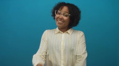 Gözlüklü gülümseyen Afrikalı Amerikalı genç bir kadın parlak mavi stüdyo ortamında x çapraz çarpıştı..