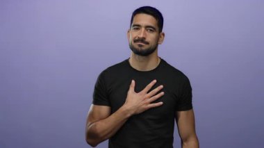 Soyutlanmış, mor bir arka plana karşı duran genç İspanyol bir adam göğsünde bir elle, samimiyet ve düşünceli duygular yayıyor..