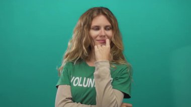 Bir kadın, yeşil tişörtlü gönüllü etiketini fırçalayan genç sarışın bir parmak tarafından stüdyoda yapılan yardım çağrısını düşünürken burnuna dokunuyor..
