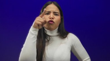 Arka planda yakalanan kadın parmağı, izole edilmiş mavi bir duvara karşı Latin kökenli genç kimliği vurguluyor..