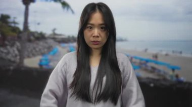 Genç Çinli bir kadın, sakin bir sahilde meditasyon yapıyor. Etrafı sakin dış mekan ortamlarıyla çevrili. Doğanın güzelliği arasında huzuru ve farkındalığı somutlaştırıyor..