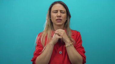 Kırmızı ceketli bir kadın, iki elini yüzüne dayayarak yanağına bastırıyor. Turkuaz bir stüdyoda, diş ağrısı için hazırlanıyor..