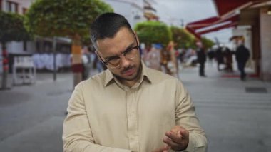 Bej tişörtlü İspanyol genç adam şehir merkezinde kalabalık bir caddede el ele veriyor..