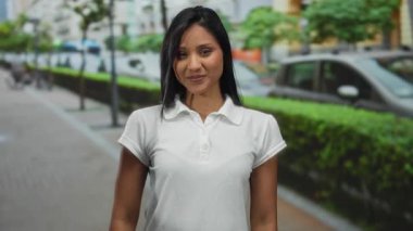 Şehir caddesinde gülümseyen bir kadın şehir hayatının özünü canlı yeşilliklerle yakalıyor, açık havada gençlik enerjisini ön plana çıkarıyor..