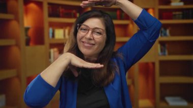 Mavi hırkalı kadın elleri ve kitaplığın önünde gülümseme ile yüzünü çerçeveler; yaratıcı vizyon sevinç.