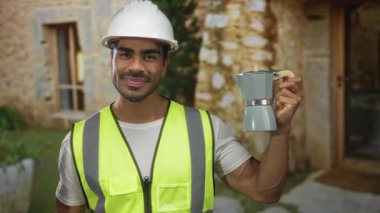 Şapka ve neon yelek giyen genç İspanyol mühendis bina girişindeki kahve makinesini işaret ediyor..
