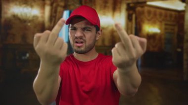 Kırmızı şapkalı ve gömlekli genç İspanyol bir adam iki orta parmağını da bir binanın içinde kaldırıyor..