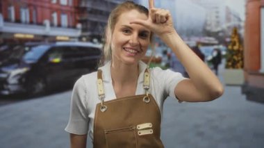 Önlük takan genç sarışın kadın işlek bir şehir caddesinde şakacı bir ezik hareketi yapıyor..