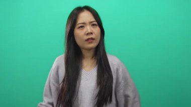 Genç Çinli bir kadın, canlı yeşil bir arka plana yaslanmış, tenha bir ortamda bıkkınlık ve bıkkınlık taşıyor..