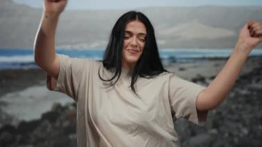 Kıvrımlı genç bir kadın sahilde tasasız bir anın tadını çıkarıyor. Kolları havada, gözleri kapalı ve sakin bir gülümseme. Sahilde dalgaların altında yavaşça yuvarlanırken..