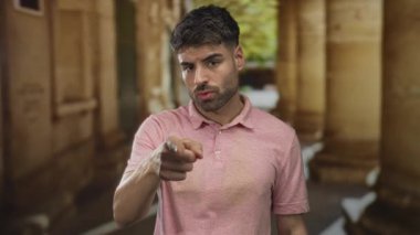 Pembe gömlekli genç adam eski kasabadaki yıpranmış taş binayı işaret ediyor..