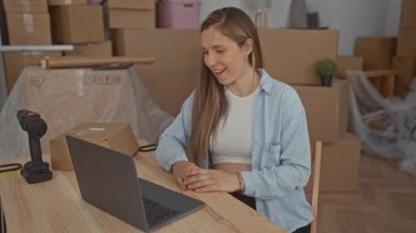 Yeni evinde, yeni bir dizüstü bilgisayarın üzerinde mutlu bir şekilde çalışan hamile bir kadın yeni bir başlangıç ve ev düzeninin altını çizerek kutular ve aletlerle çevrili..