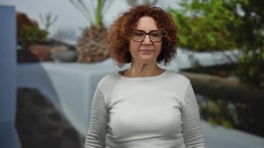 Şehir sokaklarında enerjik bir şekilde bağıran bir kadın, yapraklı arka planda, orta yaşlı esmer, gözlüklü ve beyaz bluzlu, tutkuyu ve yoğunluğu ifade eden.