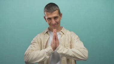 Mavi duvara karşı dua ederek gülümseyen bir adam. Stüdyoda izole edilmiş günlük gömlekler giyiyor. Huzur ve minnettarlığı simgeliyor.