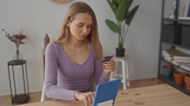 Modern oturma odasında online alışveriş için tablet kullanan bir kadın elinde kartla, dekorla, sessiz bir evin atmosferini vurguluyor.