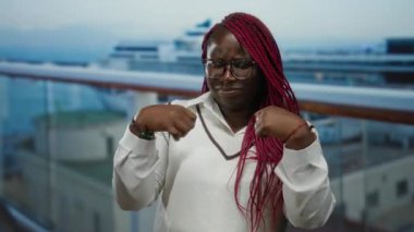 Gözlüklü ve örgülü bir kadın bileğini bir yolcu gemisinin güvertesinde acı içinde tutuyor. Arka planda deniz kenarı görünüyor. Rahatlatıcı bir yolculuk sırasında rahatsız olduğunu gösteriyor..