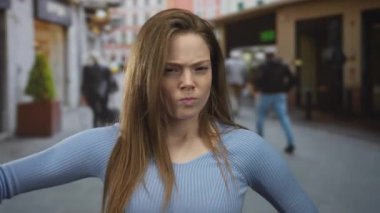 Woman shows thumb down gesture in a bustling city street scene with blurred pedestrians passing behind her; disapproval.