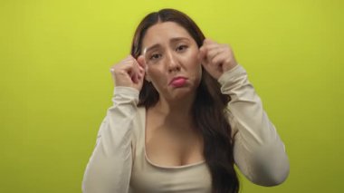 Beyaz bluzlu, uzun saçlı genç bir kadın yeşil stüdyoda dudaklarını büzüyor ve gözleriyle yumruk atıyor; üzüntü..