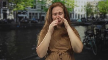 Kadın, su kanalının yanındaki sokakta burnunu sıktı ve bina cephesine yaslandı; tiksinti kaçınma.