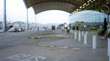 Açık hava havaalanı terminalindeki otobüsleri ve arabaları bir gölgeliğin altında görünen bireylerin bulanık görüntüsü.