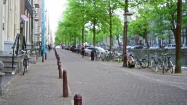 Bokeh ağaçlarıyla kaplı, arabalarla ve bisikletlerle kaplanmış, Hollanda 'nın şehir cazibesini ve hayat dolu yaşamını yakalayan Amsterdam caddesinin odaksız manzarası..