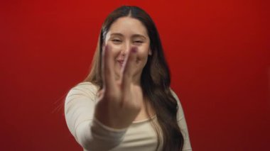 Kırmızı stüdyoda parmaklarıyla hashtag işareti yapan gülümseyen genç İspanyol kadın; hashtag trendi eğlence ifadesi.