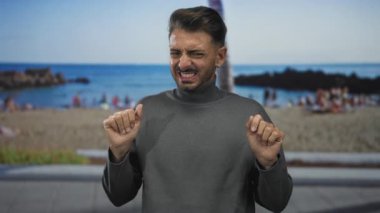 Güneşli kumlu sahilde işaret parmaklarını yukarı kaldırarak sırıtan adam, neşeli bir heyecan..